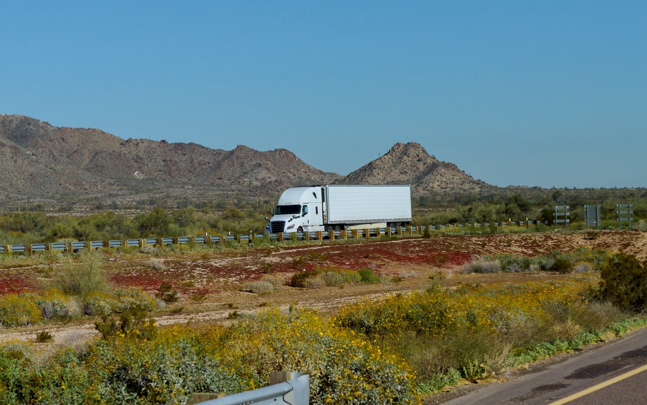 White big rig American long haul semi truck with moving on wide divided turning highway with mountain in USA
