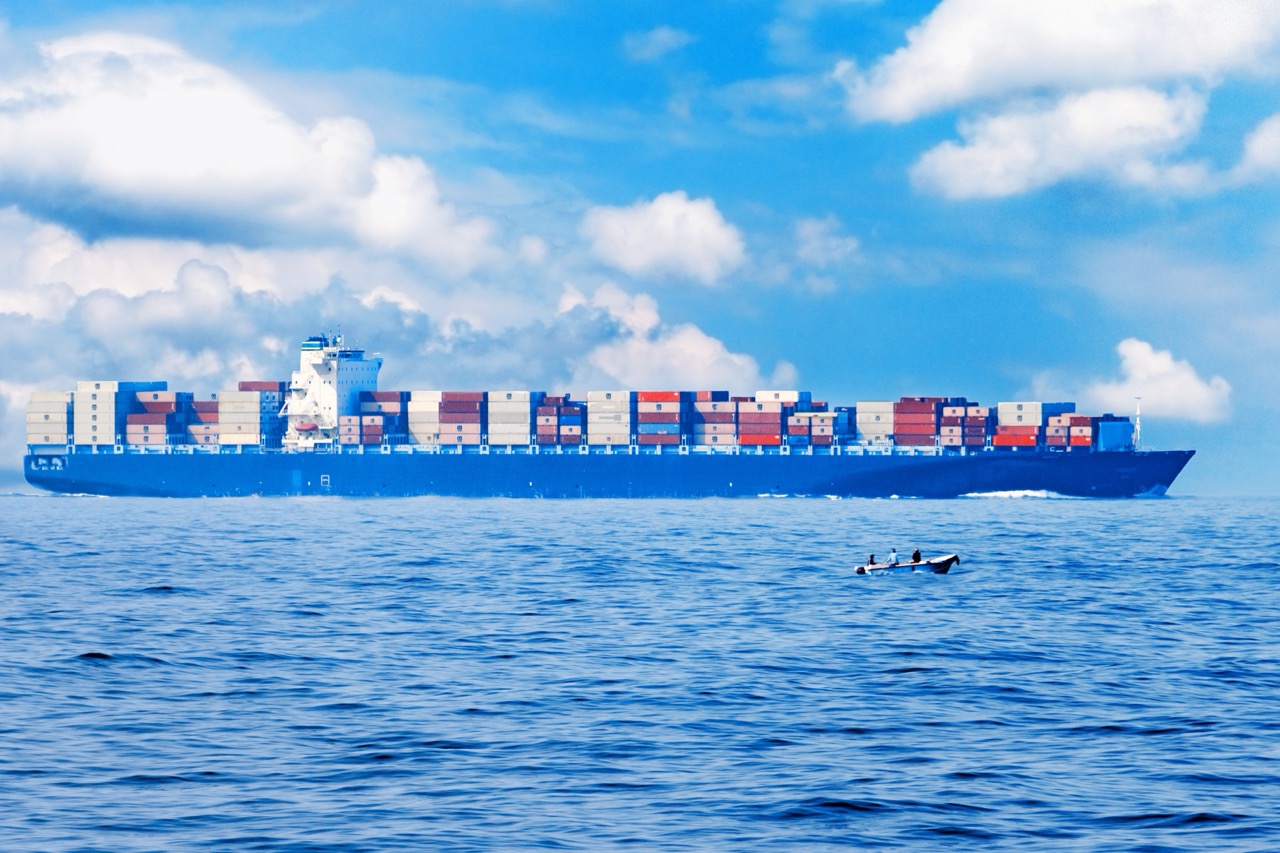 Large container cargo ship in the ocean, side view. Small fishing boat in the foreground. For logistics and transportation background.