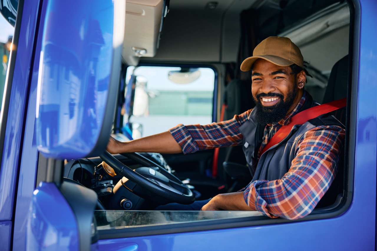 Happy black truck driver behind steering wheel in a cabin looking at camera.